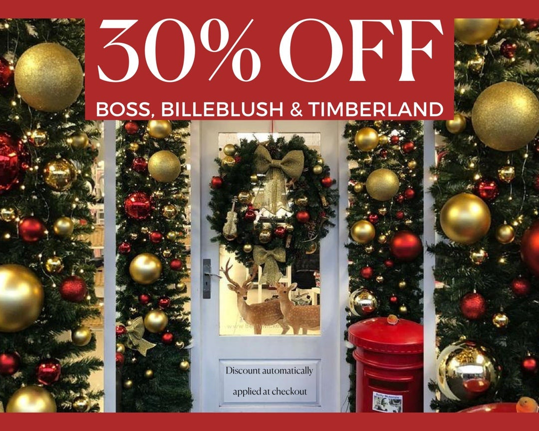 Decorative Christmas trees with gold and red ornaments in front of a store window with a discount sign.